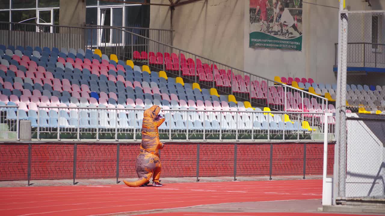 Big blow-up dragon suit outdoors. Person in a funny dragon costume running happily on the red stadium.