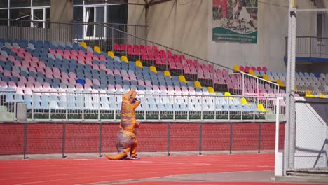 big blow-up dragon suit outdoors. person in a funny dragon costume running happily on the red stadium.