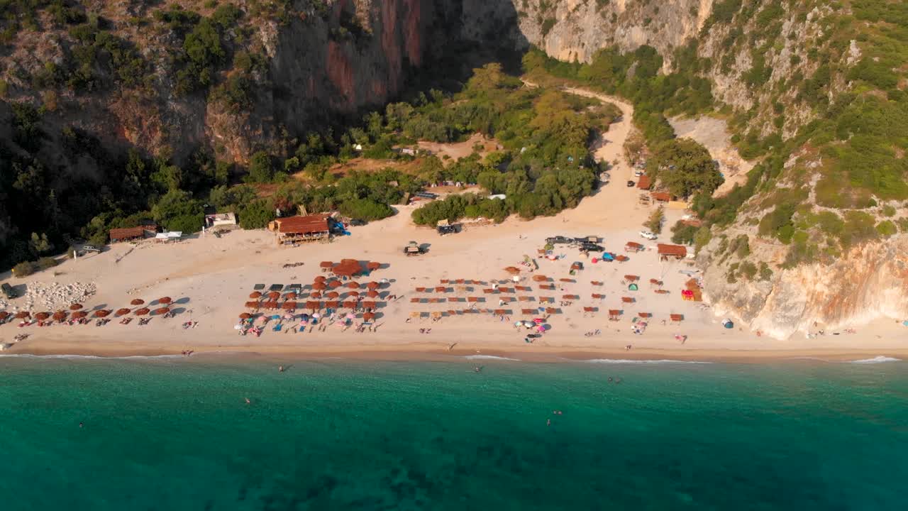 Aerial flight over beautiful hidden beach with beach umbrellas at sunset