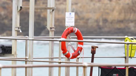 a stationary lifebuoy on a pier with ocean backdrop. bright daylight illuminates the scene, highlighting safety equipment and serene coastal environment