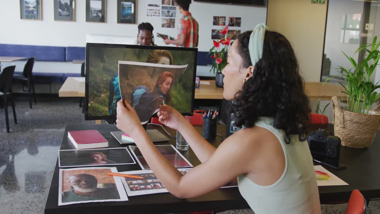 mujer de negocios biracial trabajando con una computadora portátil y sosteniendo una foto en la oficina