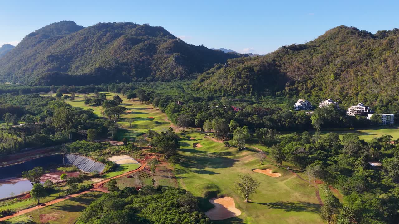 Uma tomada aérea ampla com drone revela um campo de golfe verdejante situado em meio a uma cordilheira tropical.