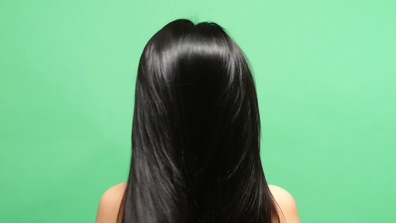 머리카락을 내려놓고 머리를 흔들고 있는 여자의 가까운 뒤쪽 시선은 녹색 스크린 배경 스튜디오에서 긴 검은색과 금발 직선 건강한 머리를 보여줍니다.