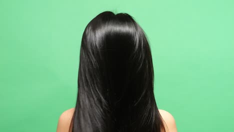 close up back view of a woman letting her hair down then shaking her head showing long black and blond straight healthy hair in the green screen background studio