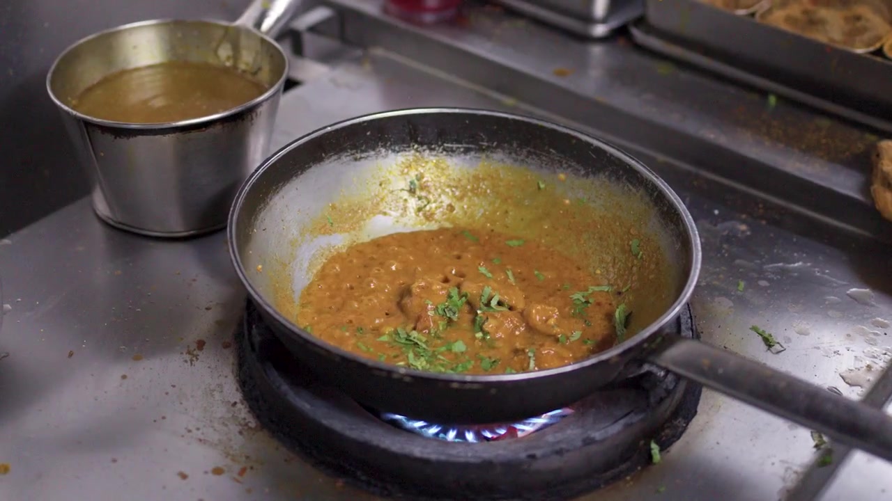 Primo piano di uno chef che aggiunge erbe fresche a un curry che sobbolle su un fornello a gas.