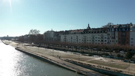 Dynamischer-Drohnenflug-über-Einem-Verschneiten-Mainz-Die-Stadt-Biontech-An-Einem-Sonnigen-Wintertag-Mit-Hochwasser-Des-Rheins-Und-Blauem-Himmel