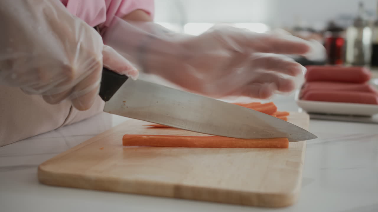 Gloved Hands of Woman Slicing Carrot at Kitchen