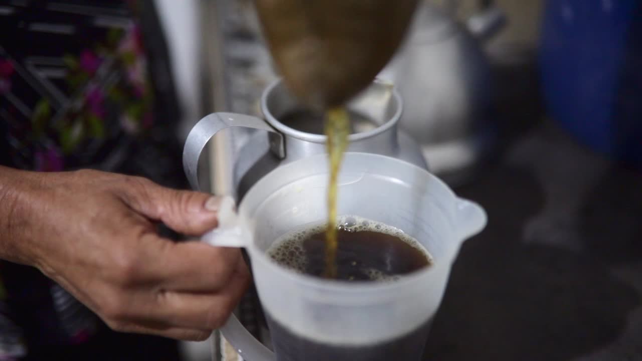 Old lady pouring a cup of hot coffee in a kitchen in Latin America