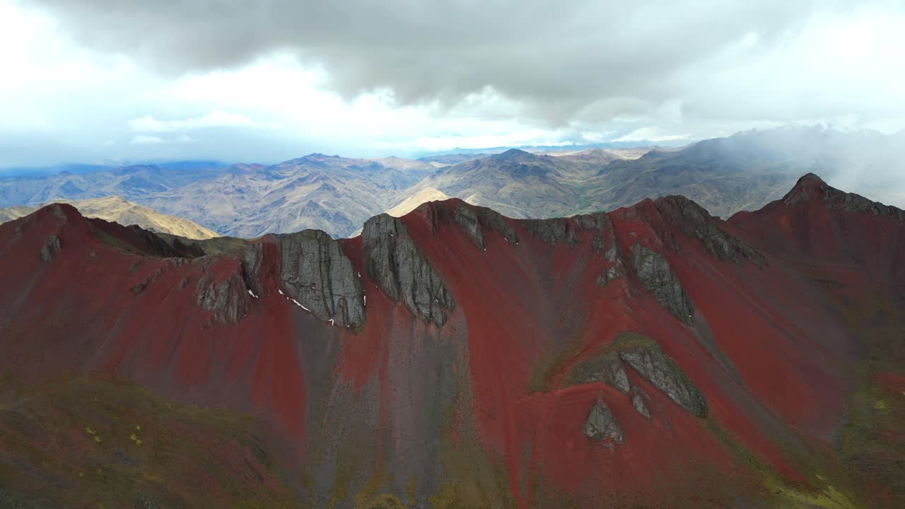 Aerial cinematic shot of Peru’s Red Mountains beneath turbulent skies. Rain and sunlight interact across the landscape in dramatic contrast