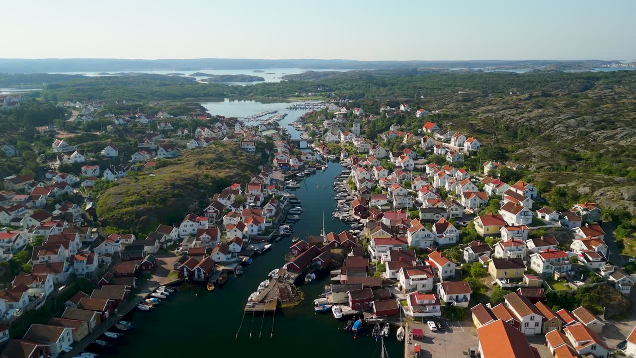 Flygfoto med parallax över Grundsund, en svensk kustby med kanal, förtöjda båtar, vita hus och klippigt skärgårdslandskap