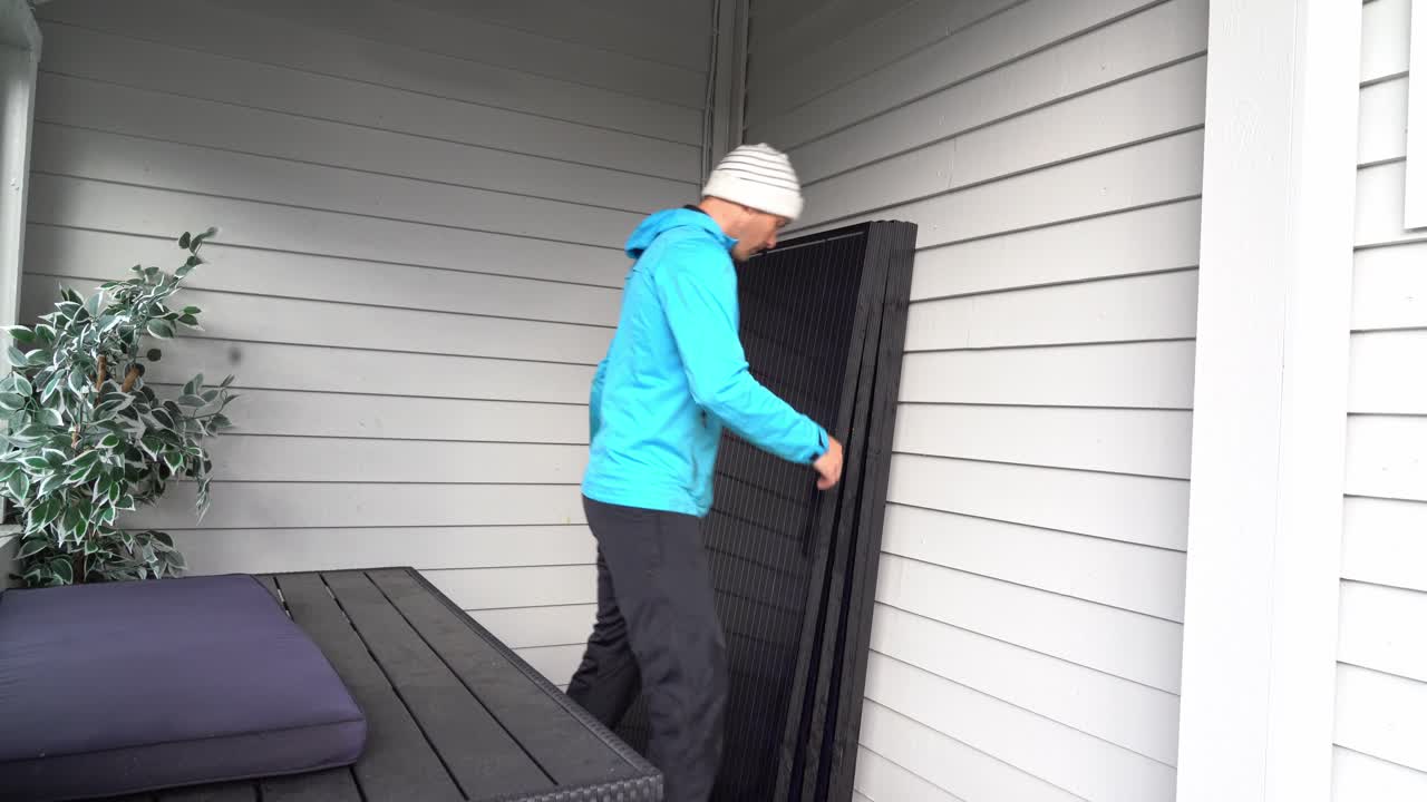 Person carrying solar panel and stacking several panels up against wall - Storing solar panels before installation on rooftop