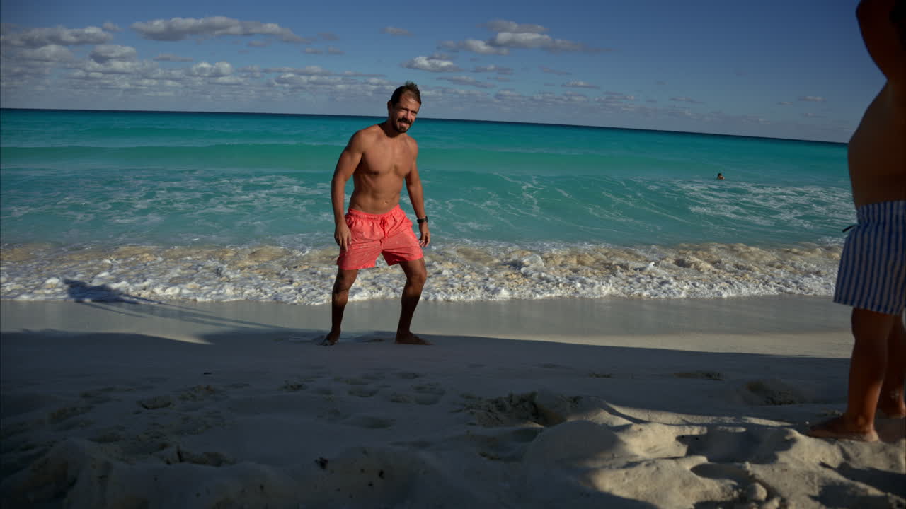 Fit mexican latin man wearing shorts showing and pointing the waves to his young son at a beach in Cancun Mexico