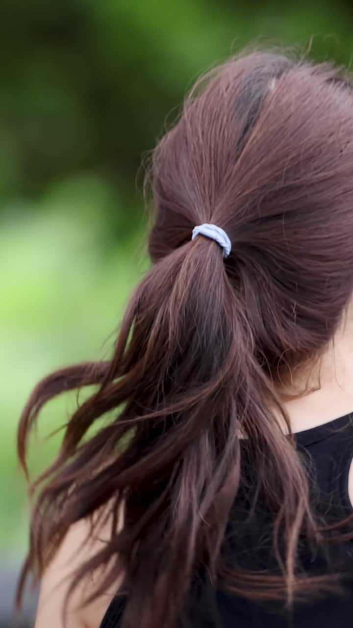 Close-up da vista traseira de uma mulher com rabo de cavalo a fazer jogging num parque verdejante e exuberante
