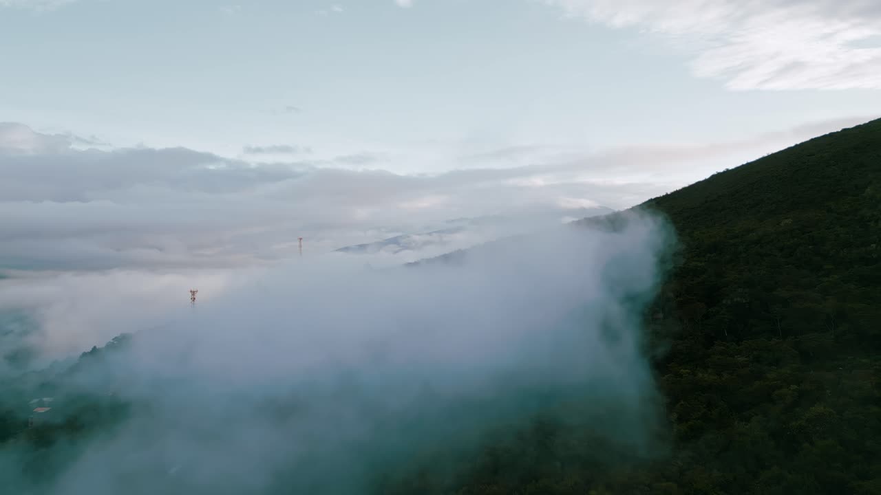 Glide above the clouds, as majestic mountain peaks emerge in the background, adorned with radio towers and providing a breathtaking backdrop to the verdant Yungas cloud forest below