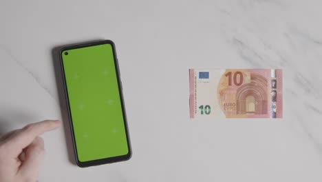 overhead currency shot of 10 euro note next to person using green screen mobile phone