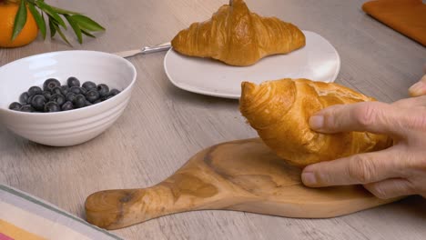 a man cuts croissants with a knife on a wooden cutting board.