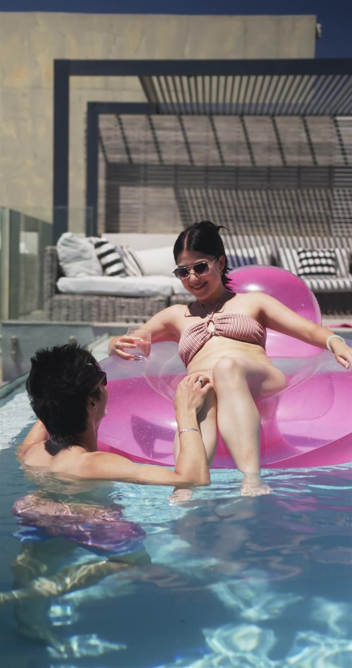 Woman on pink float reclining in pool, swimmer steadying lounger for play and causing leisure icons