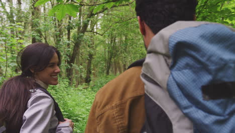 Over-the-shoulder-view-of-young-couple-hiking-along-path-through-trees-in-countryside---shot-in-slow-motion