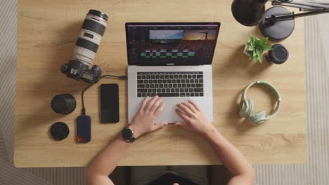 top view zoom in shot of a male editor sitting in the workspace using a laptop next to the camera editing the video at home