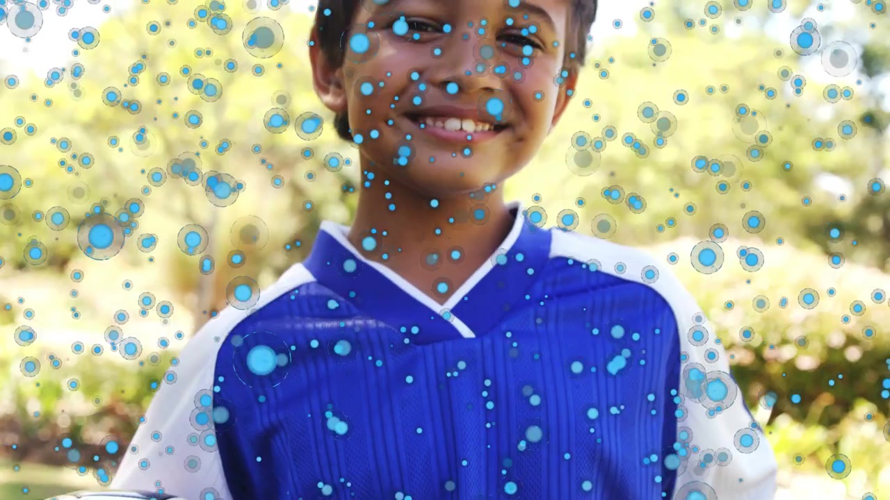 Sobreposição de partículas azuis surgindo, câmera se ampliando, revelando menino segurando bola e sorrindo para esportes