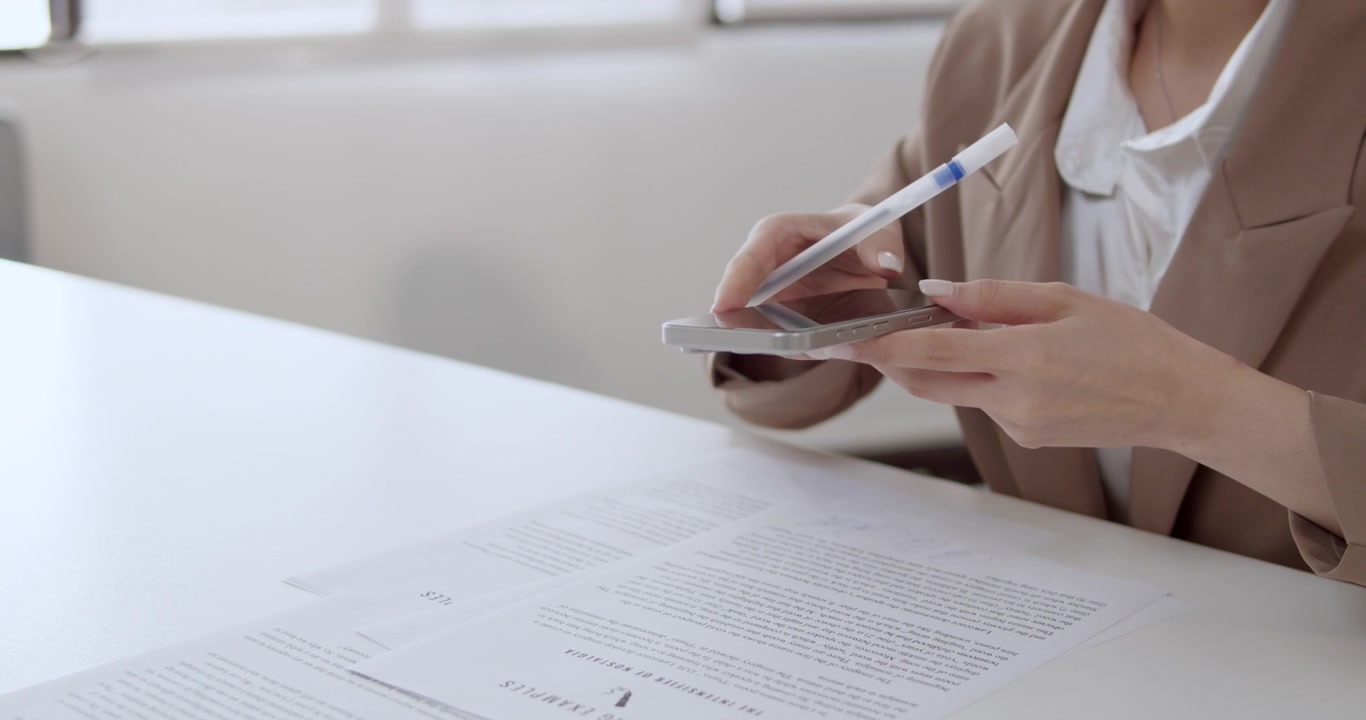 Un profesional de negocios realiza múltiples tareas utilizando un smartphone mientras revisa documentos importantes