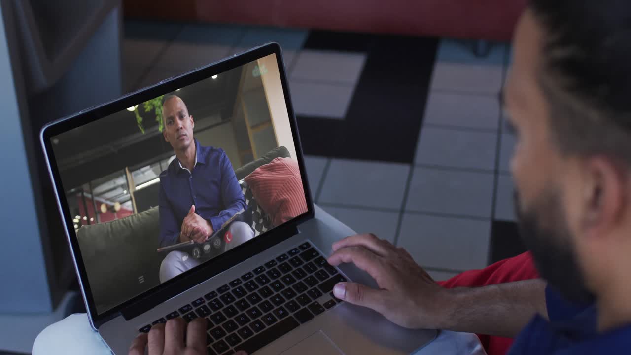 African american man having a video call with male office colleague on laptop at home