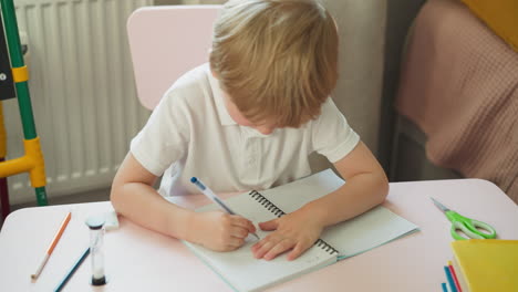 little blond pupil draws spot with pen and wipes in notebook