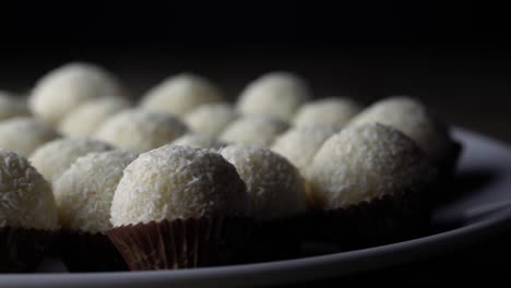 Süße-Weiße-Bällchen,-Die-Mit-Getrockneter-Kokosnuss-Bedeckt-Sind,-Sitzen-In-Kleinen-Braunen-Papiereinlagen-Auf-Einer-Weißen-Keramikplatte,-Pfanne-Rechts