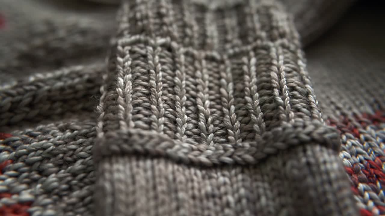On start camera panning grey knitted sleeve cuff on flat surface, revealing yarn stitch detail