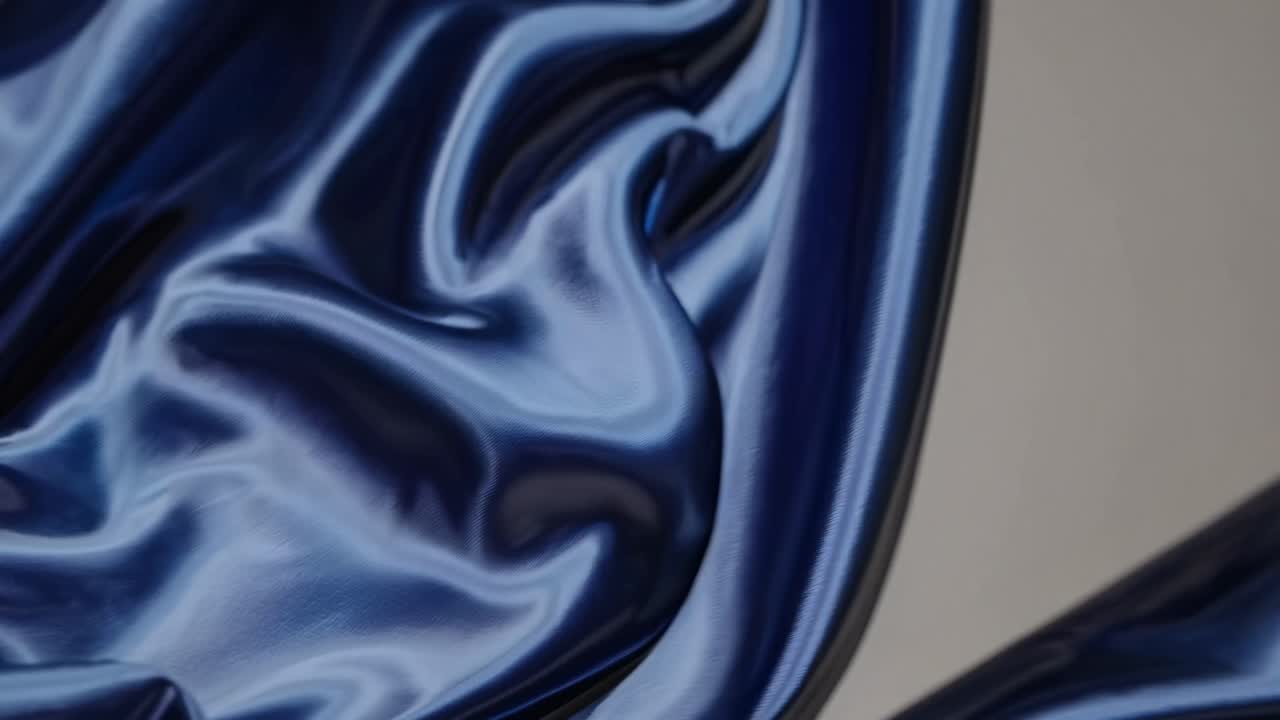 Close-up video of smooth, flowing dark blue satin fabric, capturing its glossy texture and elegant