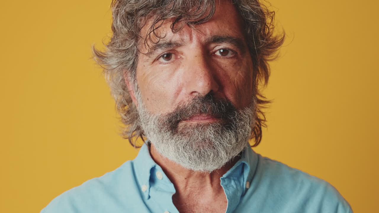 Uomo maturo con la barba che guarda seriamente in camera su sfondo giallo