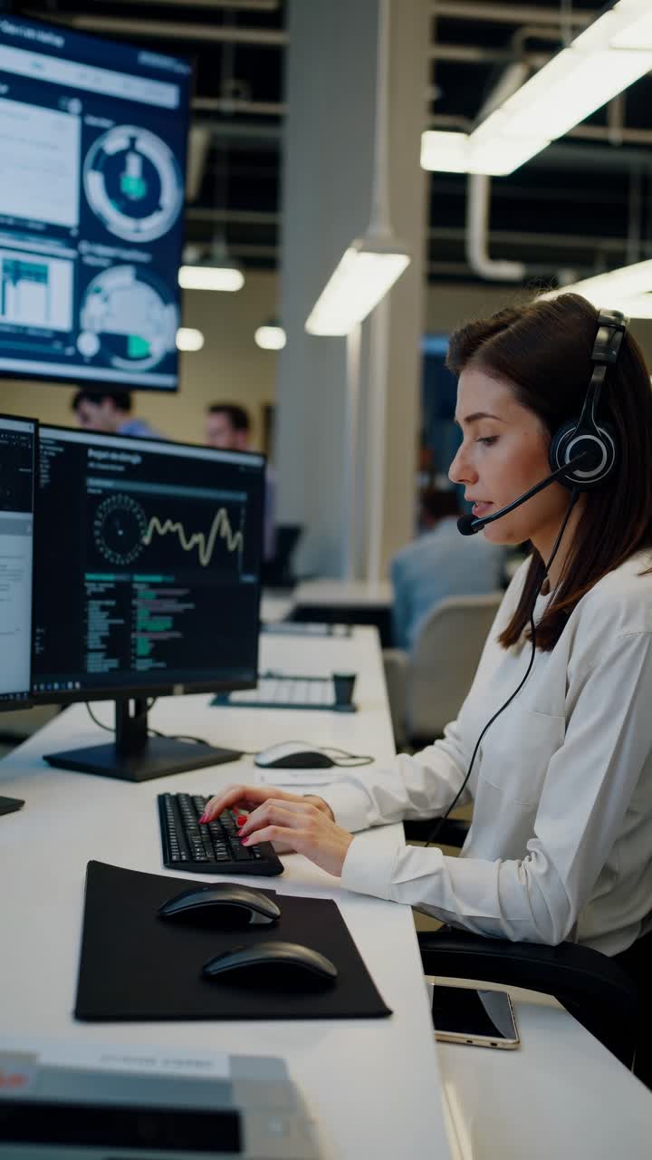 Angolazione laterale di una donna concentrata in un call center, che indossa una cuffia e lavora su due monitor.