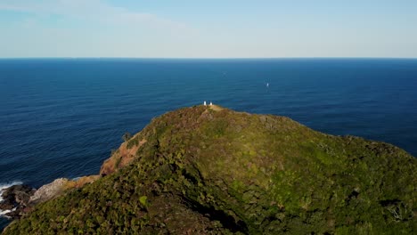 Fliegen-In-Richtung-Des-Tutukaka-Leuchtturms-Am-Bewaldeten-Berg-Vor-Einer-Ruhigen-Meereslandschaft-Auf-Der-Nordinsel,-Neuseeland