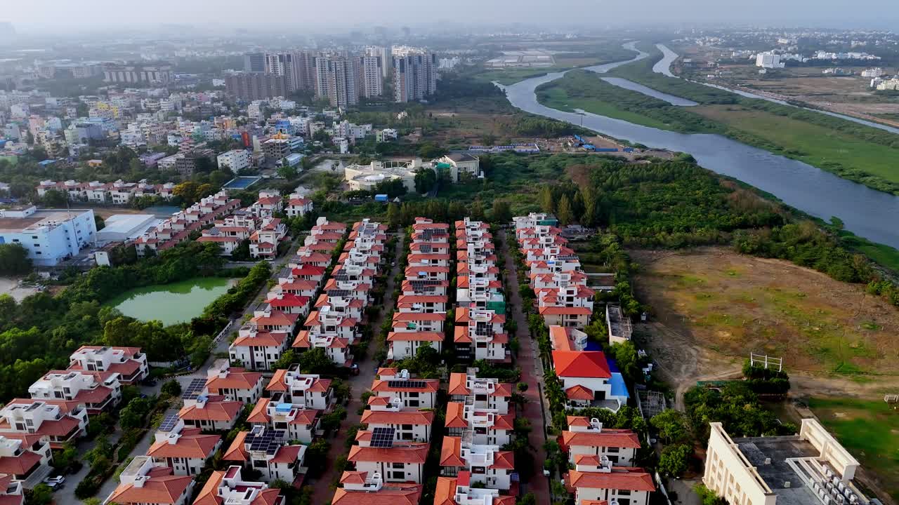 Aerial view of Chennai, India, featuring modern high-rise apartments and rows of villas with solar panels. A river flows through the expanding urban landscape.
