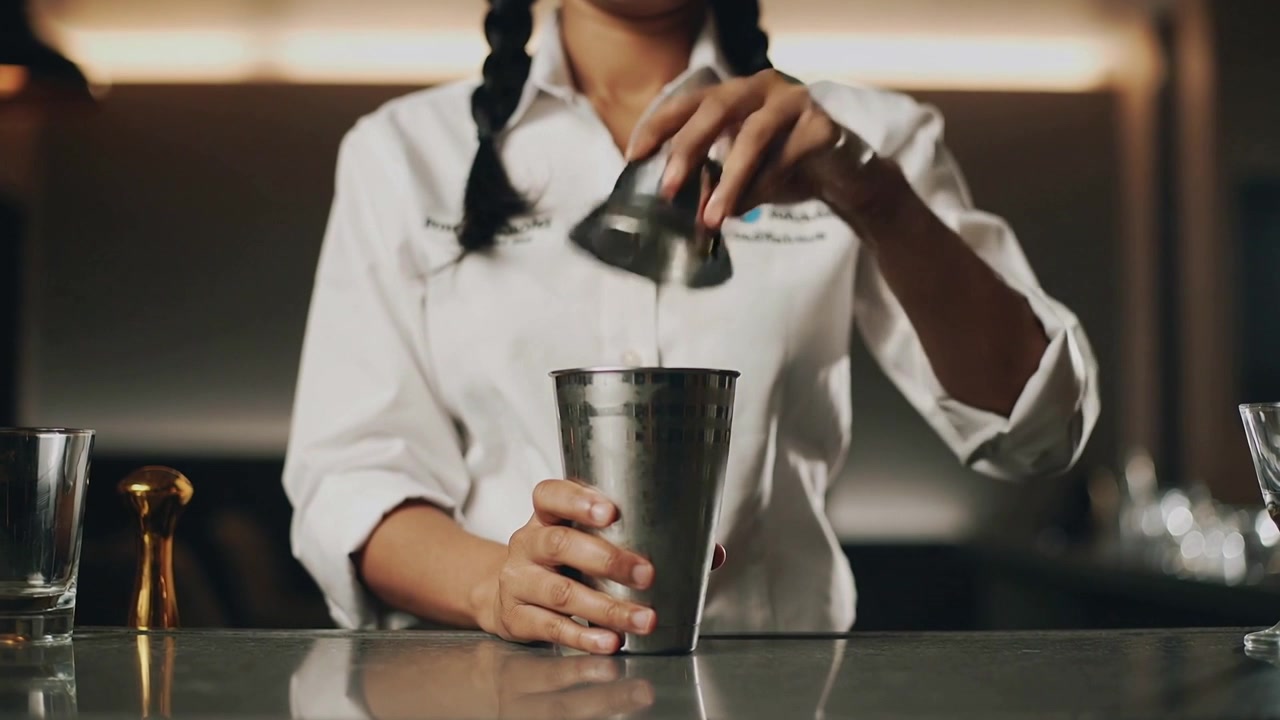 Efter bestilling forbereder bartender i hvid skjorte en cocktail ved at samle og åbne en shaker i baren