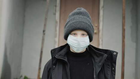 Portrait-of-a-child-from-a-poor-family.-Standing-on-the-threshold-of-his-house-in-a-protective-mask