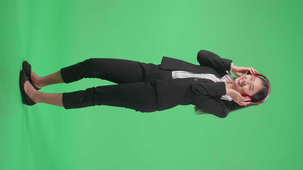 Full Side View Body Of An Asian Business Woman Listening To Music With Headphones And Dancing In The Green Screen Studio