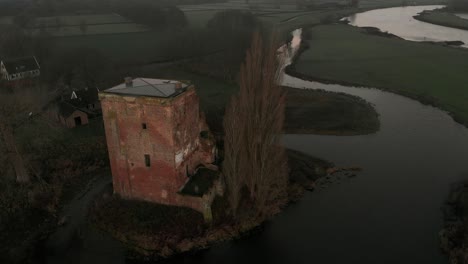 slow aerial descend showing the remains of nijenbeek castle revealing the early morning winter sunrise with ruins and tall tree in river delta landscape