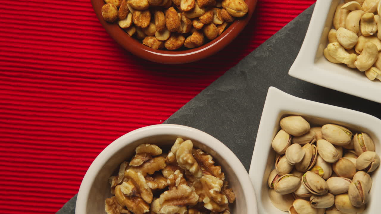 Close Up Overhead Shot Of Bowls Containing Cashews Dry Roasted Peanuts Pistachio Walnuts And Hazelnut Nuts Revolving 2