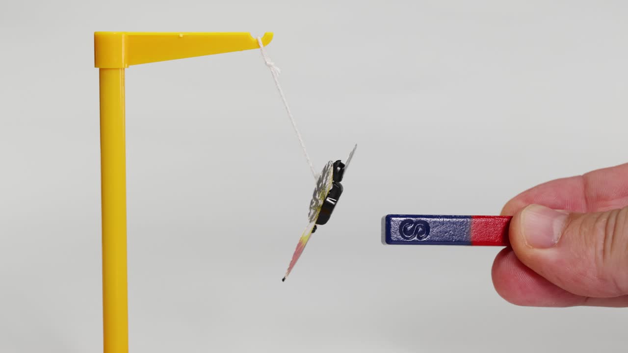 A hand manipulates a magnet near a suspended butterfly model, demonstrating magnetic attraction and repulsion in a controlled environment