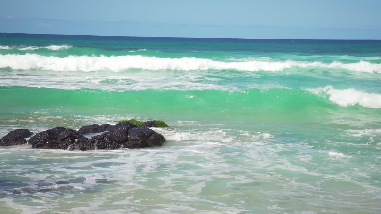 Close-up of waves crashing on rocky sections at Cabarita Beach. The stunning aqua waters of this pristine location highlight the raw power of nature against the rocky shore.