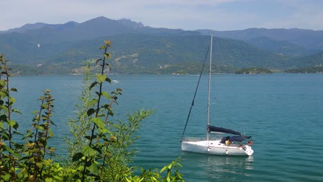 Botes-Blancos-Flotando-En-La-Laguna-Oceánica-Con-Cubierta-Montañosa,-Agua-Azul-Del-Océano-Sin-Gente,-Hojas-Verdes-De-Arbustos-En-La-Playa-Costera