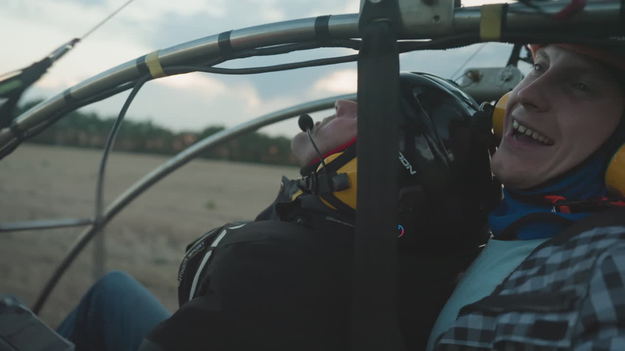 closeup of excited man in helmet and goggles gripping paramotor cage with open mouth as engine revs against blurred sky and field background moments before flight takeoff