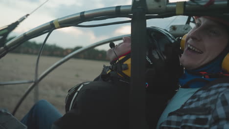 closeup of excited man in helmet and goggles gripping paramotor cage with open mouth as engine revs against blurred sky and field background moments before flight takeoff