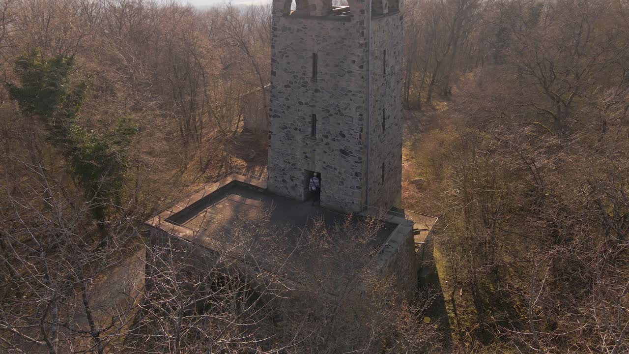 toma aérea estática a través de un árbol desnudo de un joven explorando el primer nivel de la torre wetzlar