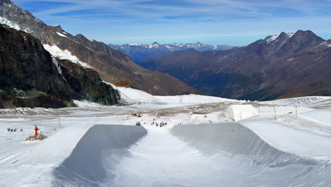 Summer-Autumn-Fall-training-halfpipe-snowboarding-ski-The-Stomping-Grounds-aerial-drone-flight-Saas-Fee-Saastal-ski-resort-glacier-sunny-bright-beautiful-blue-sky-high-clouds-slush-ice-pan-down-reveal