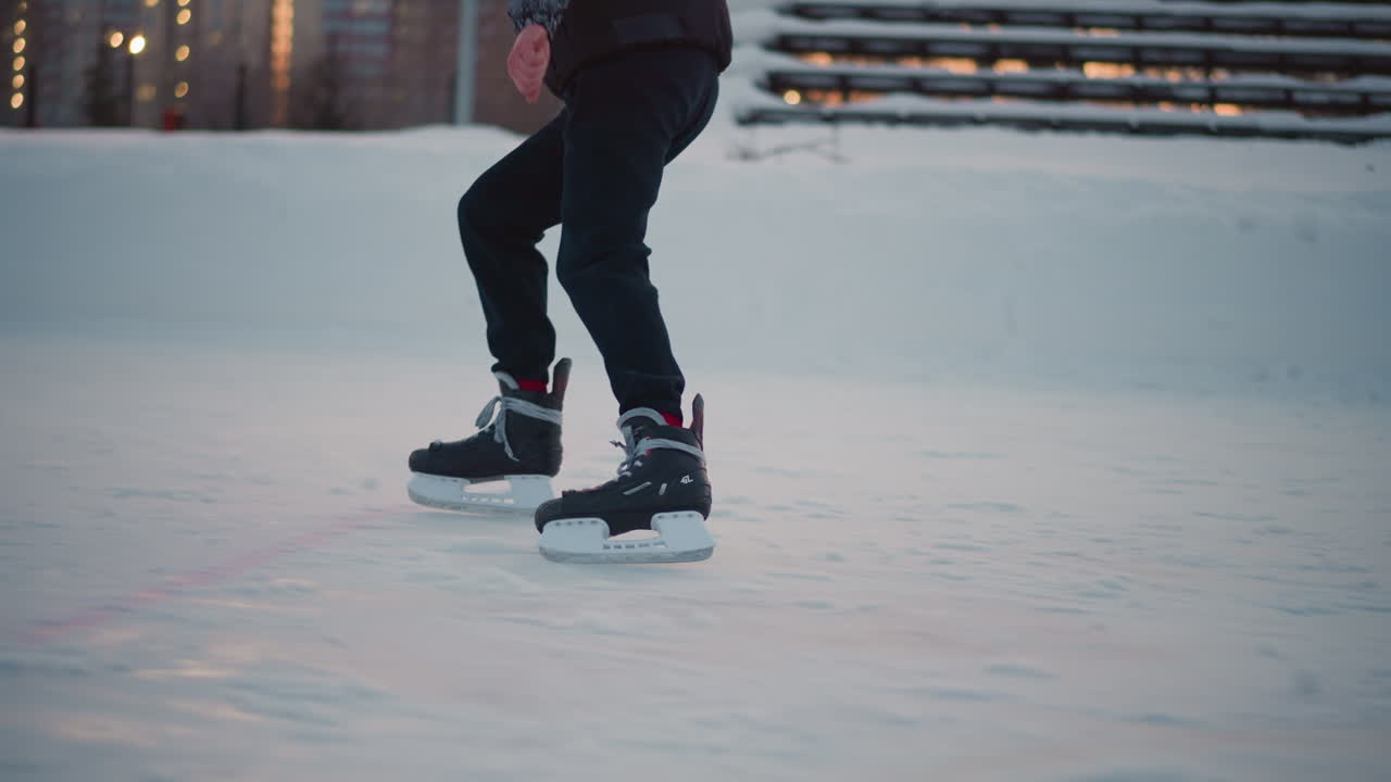 side view young boy skating skillfully on ice rink outdoor hockey field at sunset golden sunlight reflecting on ice smooth glide blurred building background crisp winter atmosphere motion