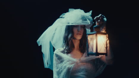 woman in white dress and veil holding a lantern in darkness