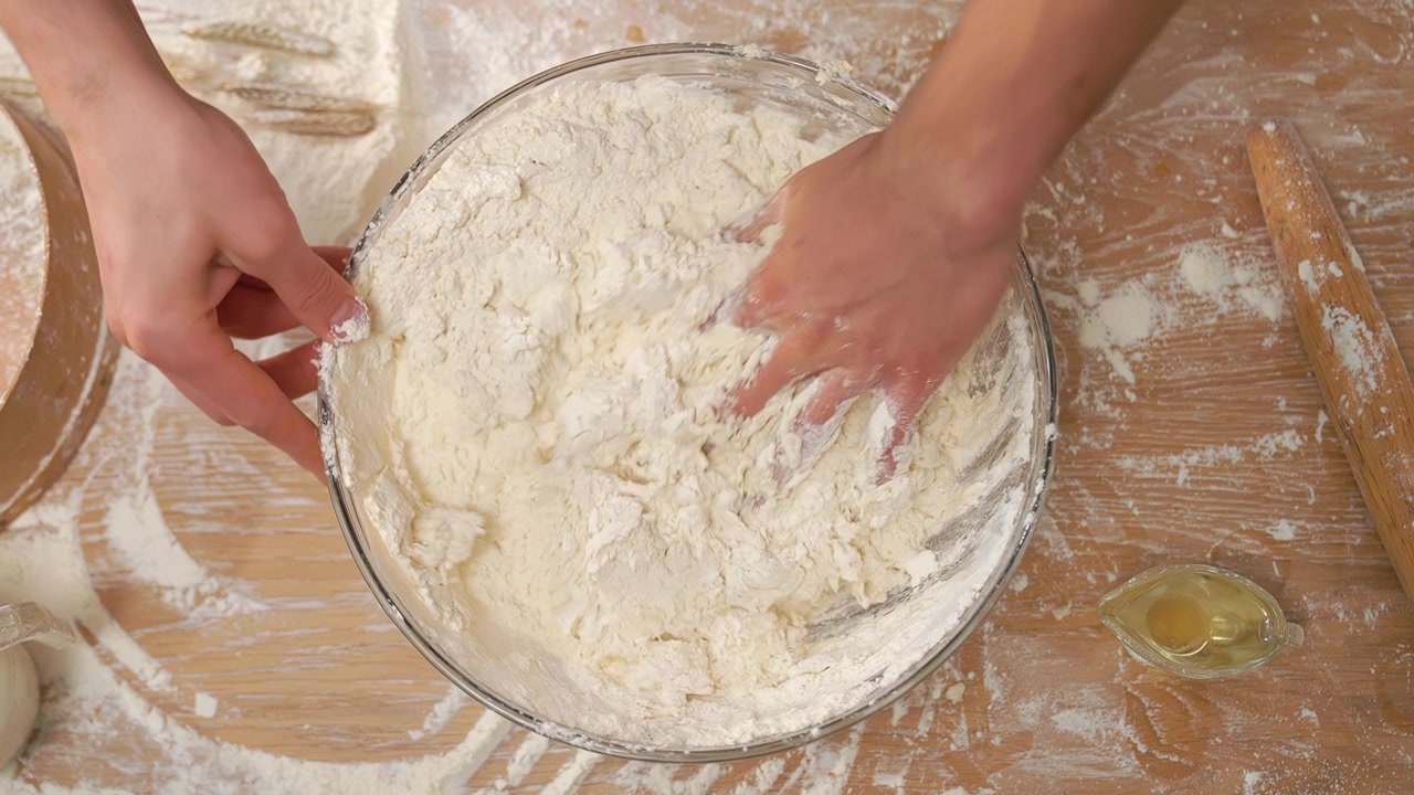Person's Hands Mixing Dough in a Bowl on a Floured Wooden Table