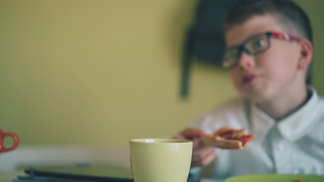 un ragazzo in camicia pranza con una pizza vicino a un compagno di classe in mensa.